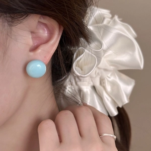 Gros plan de boucles d'oreilles rondes bleu menthe portées par un mannequin en été