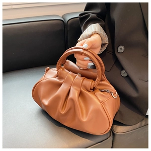 Detail of a brown pleated cloud bag with a circular handle and gold metal zipper hardware