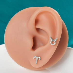 Macro shot of silver zodiac earrings with white cubic zirconia on a silicone ear model