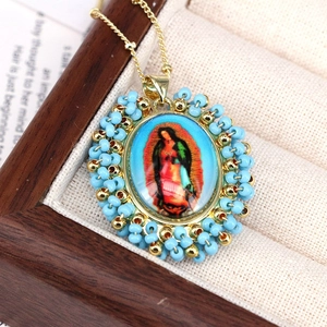 Close-up of Virgin Mary oval pendant with blue beads and golden chain in a jewelry box