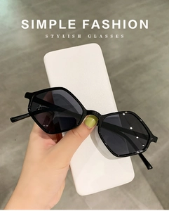 Detail of hand holding black hexagonal sunglasses with dark lenses and simple white case