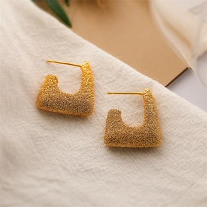 Macro shot of gold geometric earrings with a brushed texture on white textured fabric