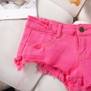 Dettaglio degli shorts in denim rosa con orli sfilacciati e bottone in metallo