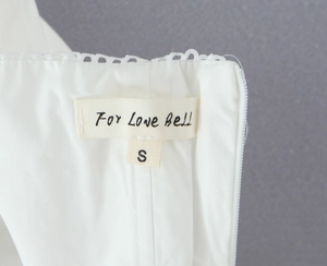 Detail of white halter dress neckline showing S size tag and embroidered eyelet texture