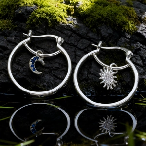 Détail macro de créoles soleil et lune en argent avec zircon bleu sur roche moussue