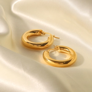 Close-up of chunky gold hoop earrings on elegant beige silk fabric with soft light