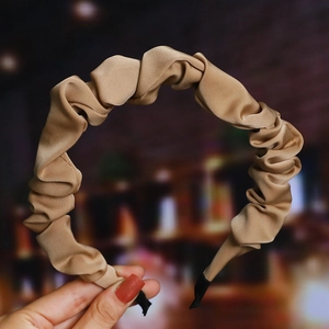 Close-up of pleated satin headband in champagne gold with elegant silky texture