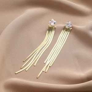 Detail showing long golden fringe earrings with square-cut crystal and sleek snake chains