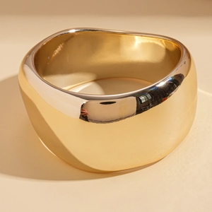 Close-up of a wide wavy gold polished cuff bracelet with a glossy metallic finish
