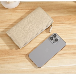 Beige pebble leather long wallet next to a smartphone for size scale on wooden desk