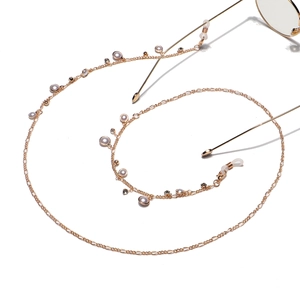 Chaîne à lunettes dorée avec perles blanches et accents de cristal sur fond blanc
