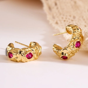 Gold plated C-shape earrings with red zircon stones and embossed texture on lace background