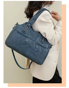Detail of soft leather tote bag showing textured blue-grey material and metal zippers