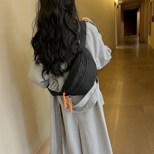 Minimalist black canvas chest bag with orange zipper pull and adjustable strap