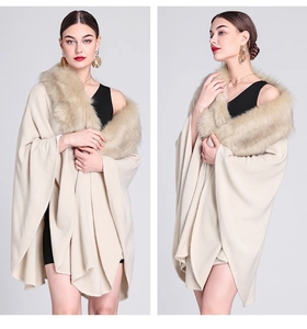 Detail of a beige knitted poncho with faux fox fur collar on a female model