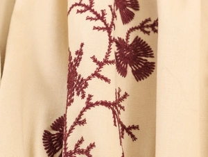 Close-up of deep red floral embroidery patterns on beige long sleeve dress fabric