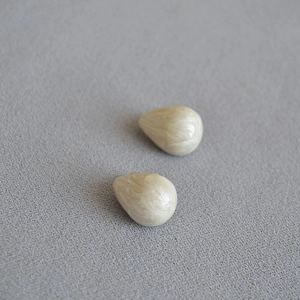 Detail of tear-drop shaped enamel earrings with creamy marble texture and gold plating