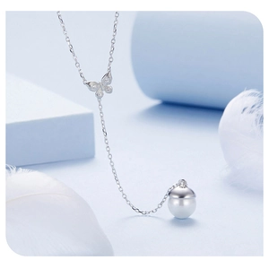 Detail view of silver butterfly necklace with white pearl pendant on soft background