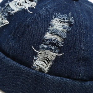 Detailed macro view of distressed denim fabric with frayed edges on a brimless docker cap