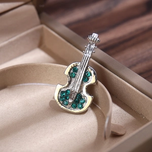 Close-up of a silver violin brooch with inlaid green gemstones in a beige gift box