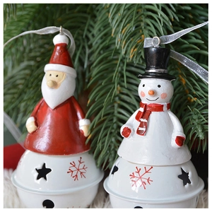Detail of red Santa and white snowman Christmas bells hanging on a lush green tree branch
