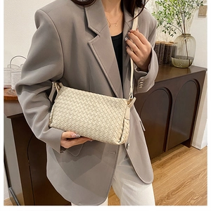 Détail du sac bandoulière en cuir tressé crème avec blazer gris et décor intérieur