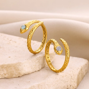 Detail of gold snake rings with scale texture and blue gemstone on stone base