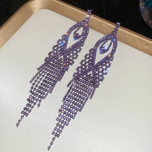 Detailed macro view of sparkling purple rhinestone tassel earrings on a golden tray