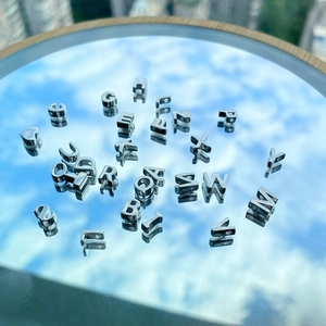 Detail shot of S925 silver letter charms and heart pendants on a reflective mirror surface