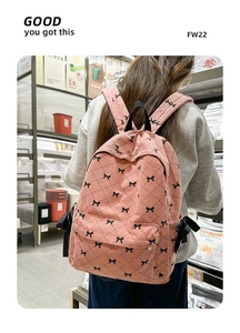 Rear view of a pink corduroy backpack with bow patterns in a lifestyle supermarket setting