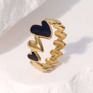 Macro detail of gold stainless steel ring with black enamel hearts on textured stone
