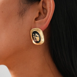 Détail d'une boucle d'oreille ovale dorée avec un relief de calèche en émail noir