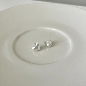 Close-up of S925 sterling silver heart studs with a brushed finish on a ceramic plate