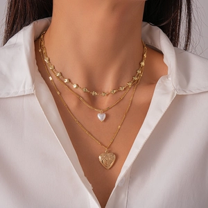 Detailed close-up of triple-layered golden necklace with heart charms and faux pearls
