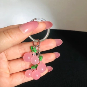 Close-up of pink resin cherry keychain with silver ring held by a hand in detail