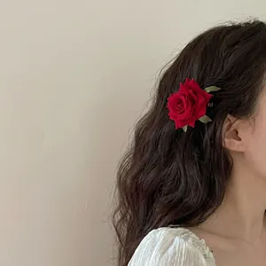 Detail of a realistic red velvet rose hair clip with green leaves in a curly hairstyle