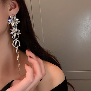 Close-up of sparkling silver tassel earrings with flower studs worn by a model