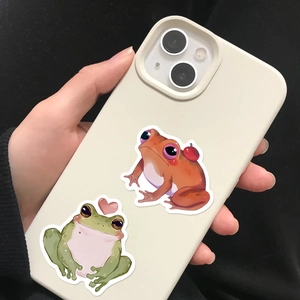 Close-up of cute cartoon frog stickers on white phone case with heart and apple themes