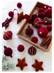Flat lay of velvet Christmas ornaments with red ribbons and pine on snowy base