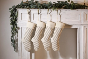 Detail of four knitted Christmas stockings with cream diagonal stripes hanging on fireplace
