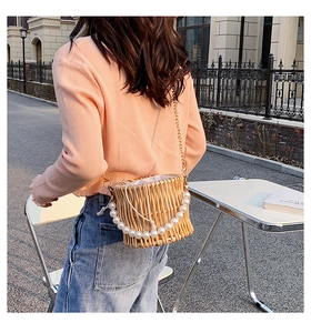 Detail of hand-woven straw bucket bag with large pearl handle and gold chain strap