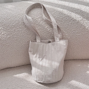Detail van beige geplooide shopper met fijne textuur en dunne riempjes op zachte achtergrond