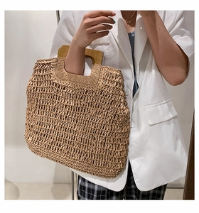 Detail of straw woven tote bag featuring a square dark wood handle and natural texture