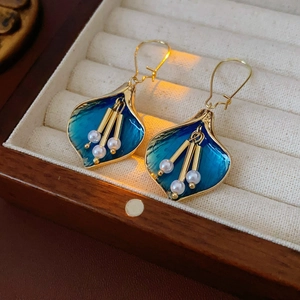 Détail de boucles d'oreilles feuilles bleues avec bords dorés et pompons de perles