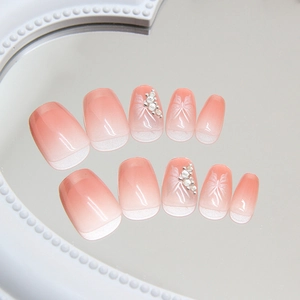 Faux ongles ombré rose et blanc avec ailes de papillon et perles sur un miroir
