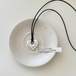 Minimalist silver heart pendant on black cord necklace displayed on white ceramic plate