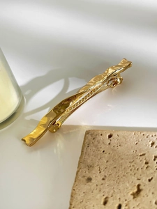 Detail view of a wavy gold metal hair clip with a polished finish and duckbill structure