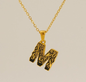 Macro detail of 18k gold letter M pendant with vintage textured black engravings