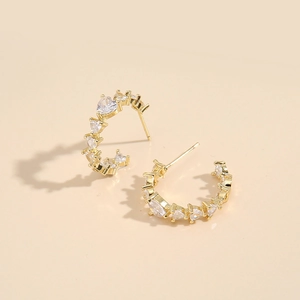 Golden C-shaped hoop earrings with heart-shaped zircon stones on a beige background