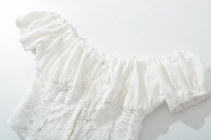 Detail of white lace blouse featuring ruffled neckline, drawstring bow, and puff sleeves